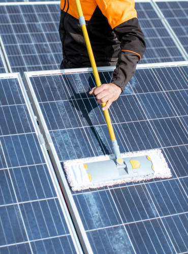 Technicien nettoyant des panneaux solaires avec un balai spécial