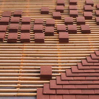 Close-up of red clay tiles being placed on a roof, showcasing construction and craftsmanship.